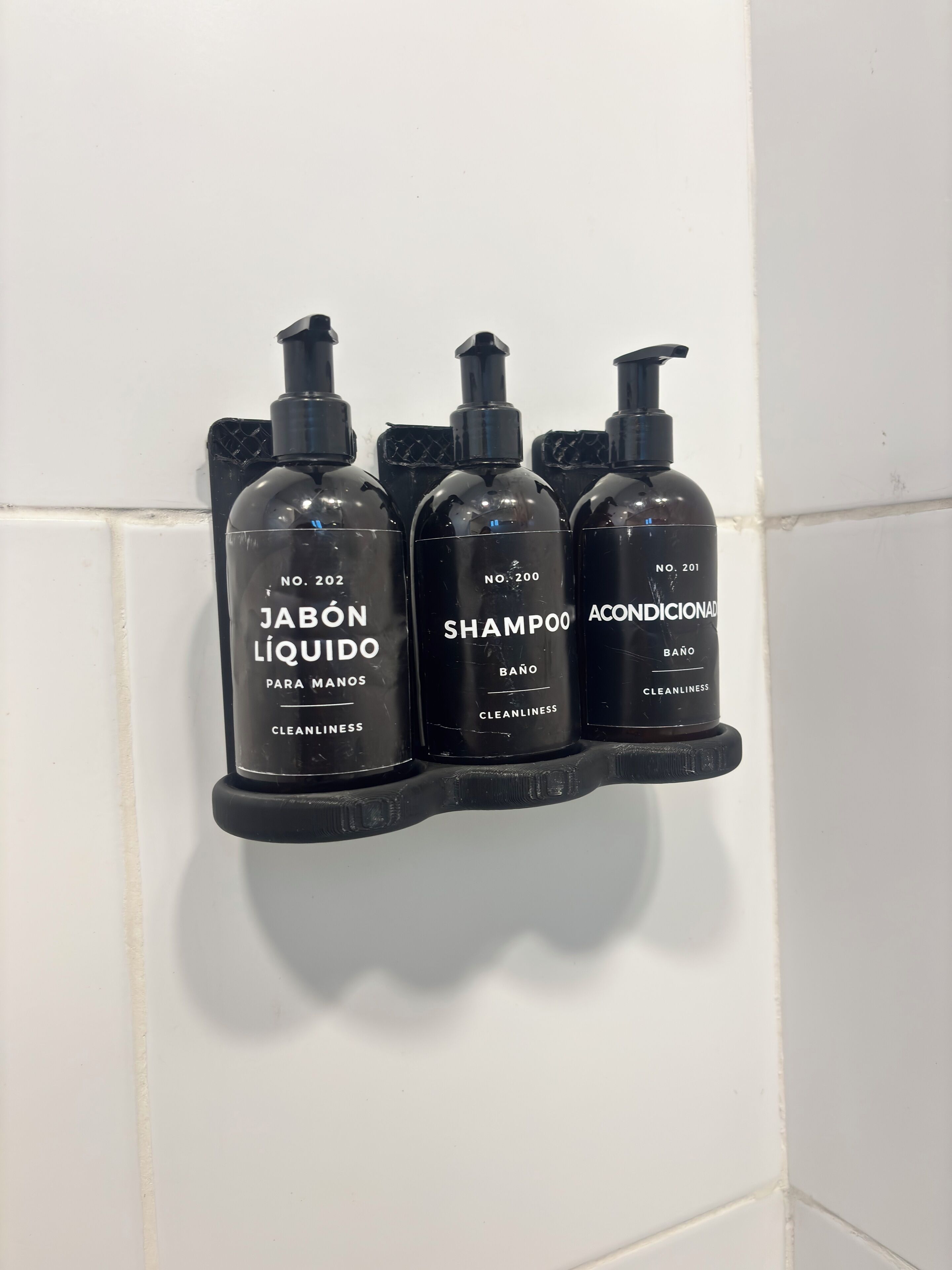 Three black bottles of personal care products on a white tiled wall.