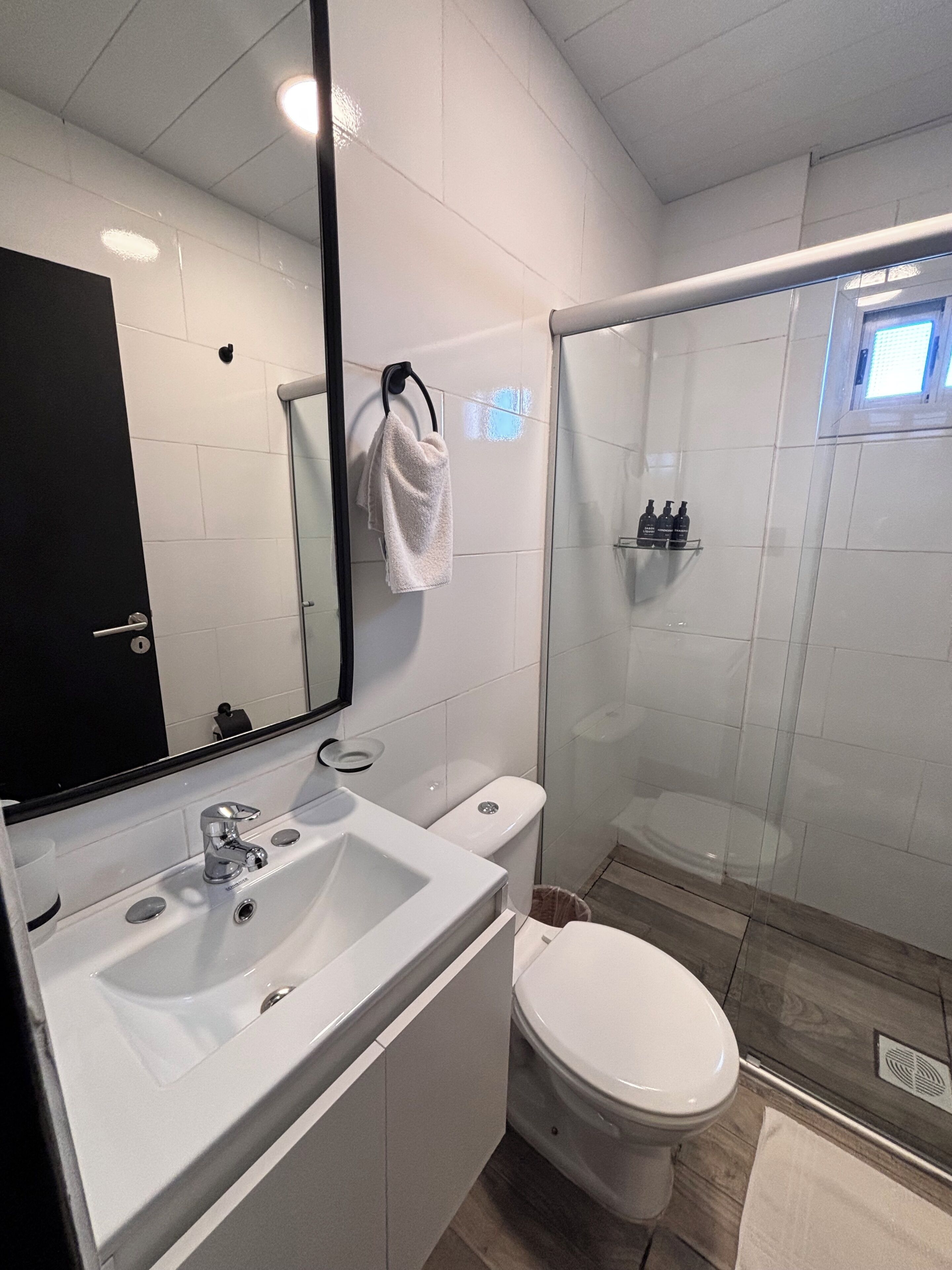 Un baño moderno con lavamanos, espejo e inodoro blancos.