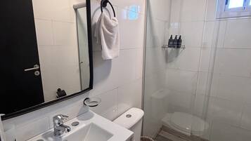 Un baño moderno con lavamanos, espejo e inodoro blancos.