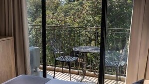 Een hotelkamer met een groot bed, een balkon met een tafel en stoelen, en uitzicht op bomen.
