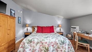 A bedroom with a floral bedspread, a wooden wardrobe, a desk with a chair, and a wall-mounted air conditioner.