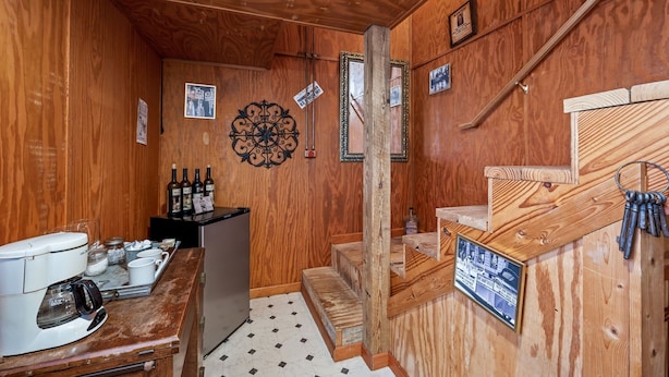Een houten interieur met een koffieapparaat, een kleine koelkast en een houten trap.