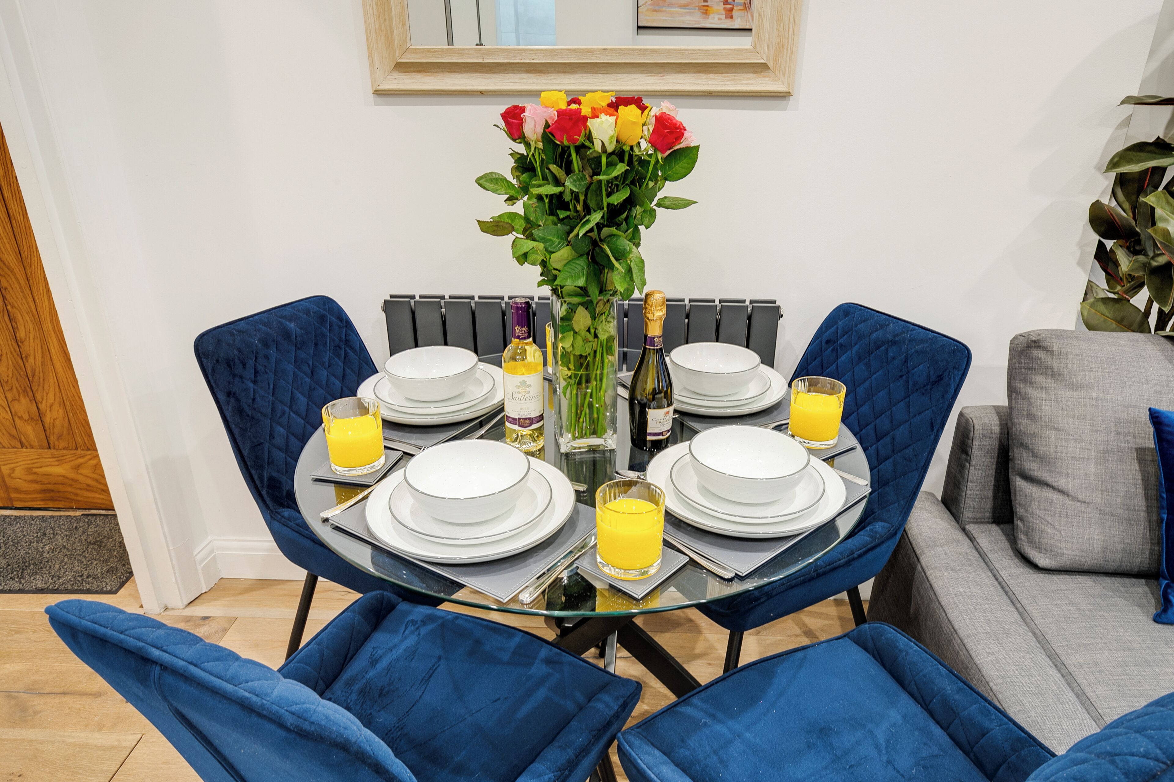 A dining table set with plates, glasses, and a bottle of champagne, surrounded by blue chairs.