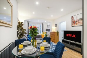 A modern living room with a dining area, a TV displaying 'NETFLIX', and a large window with a view of the city. - Perfect Large Studio bedroom apartment in tranquil London neighbourhood (London)