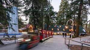 Un tren rojo avanzando por un paisaje nevado con un edificio al fondo.
