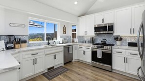 Una cocina moderna con armarios blancos, electrodomésticos de acero inoxidable y un ventanal con vistas al exterior.