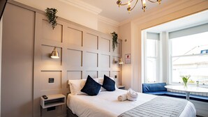 A hotel room with a large bed, bedside tables, a wall-mounted lamp, a window with a view, and a small table with flowers. - Howth Marina Escape (Howth)