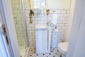 Een badkamer met een wit wastafel, toilet en douche. Er staan planten op de muur en een handdoek hangt aan de zijkant.