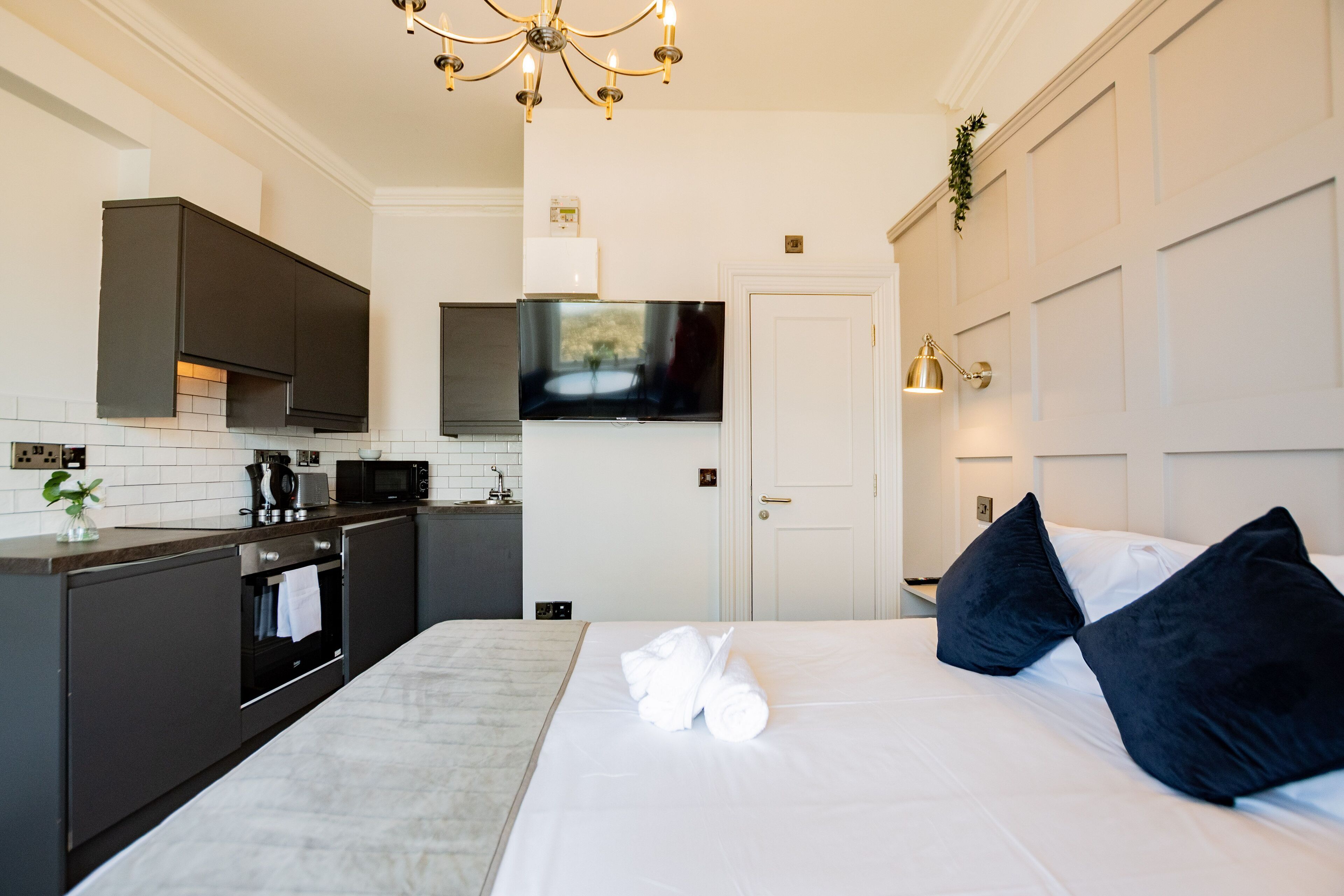 A modern hotel room with a large bed, dark-toned headboard, and a flat-screen TV mounted above the bed.