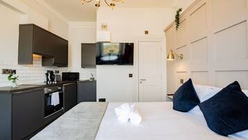 A modern hotel room with a large bed, dark-toned headboard, and a flat-screen TV mounted above the bed.