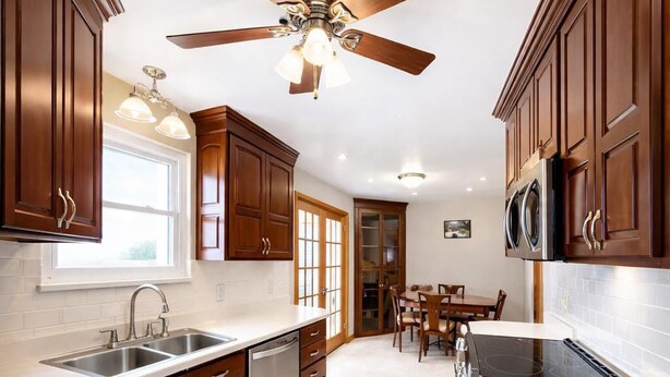 Une cuisine avec des meubles en bois, un ventilateur de plafond, un lave-vaisselle et un coin repas comprenant des chaises et une table.