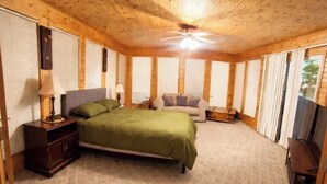Une chambre à coucher comprenant un lit, une table de chevet, une commode, un ventilateur de plafond et une fenêtre avec des stores.