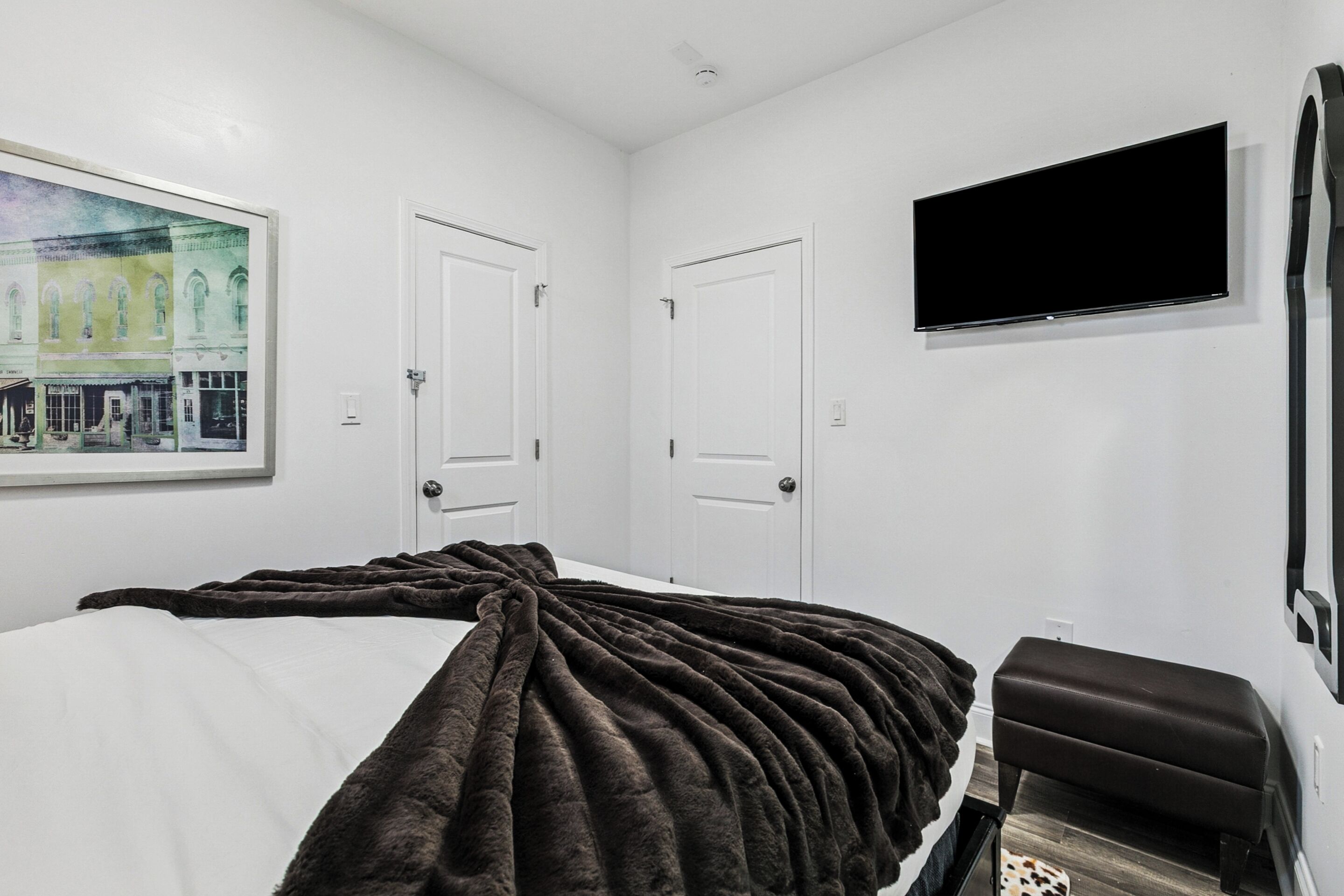 Une chambre à coucher avec un lit, un grand tableau, deux portes, un téléviseur à écran plat et un banc.