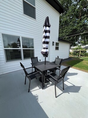 A patio with a table and chairs, an umbrella, and a house in the background. - Husker Getaway lV (Lincoln)