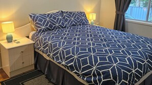 A bedroom with a bed, nightstands, a lamp, a ceiling fan, a window with curtains, and a view of the outdoors. - Bribie Beach Shack close to the bridge! (Bongaree)