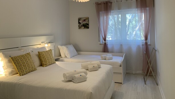 Een hotelkamer met twee bedden, een plafondlamp, een raam met gordijnen, en een klein kunstwerk aan de muur.