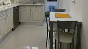 Een moderne keuken met witte kasten, een eettafel met stoelen en een hanglamp.