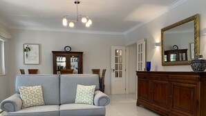 Een woonkamer met een grijze bank, een bijzettafeltje, een houten kast en een kroonluchter.