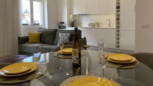 Ett modernt vardagsrum med ett matbord i glas för fyra personer, en soffa med kuddar och ett kök i bakgrunden.