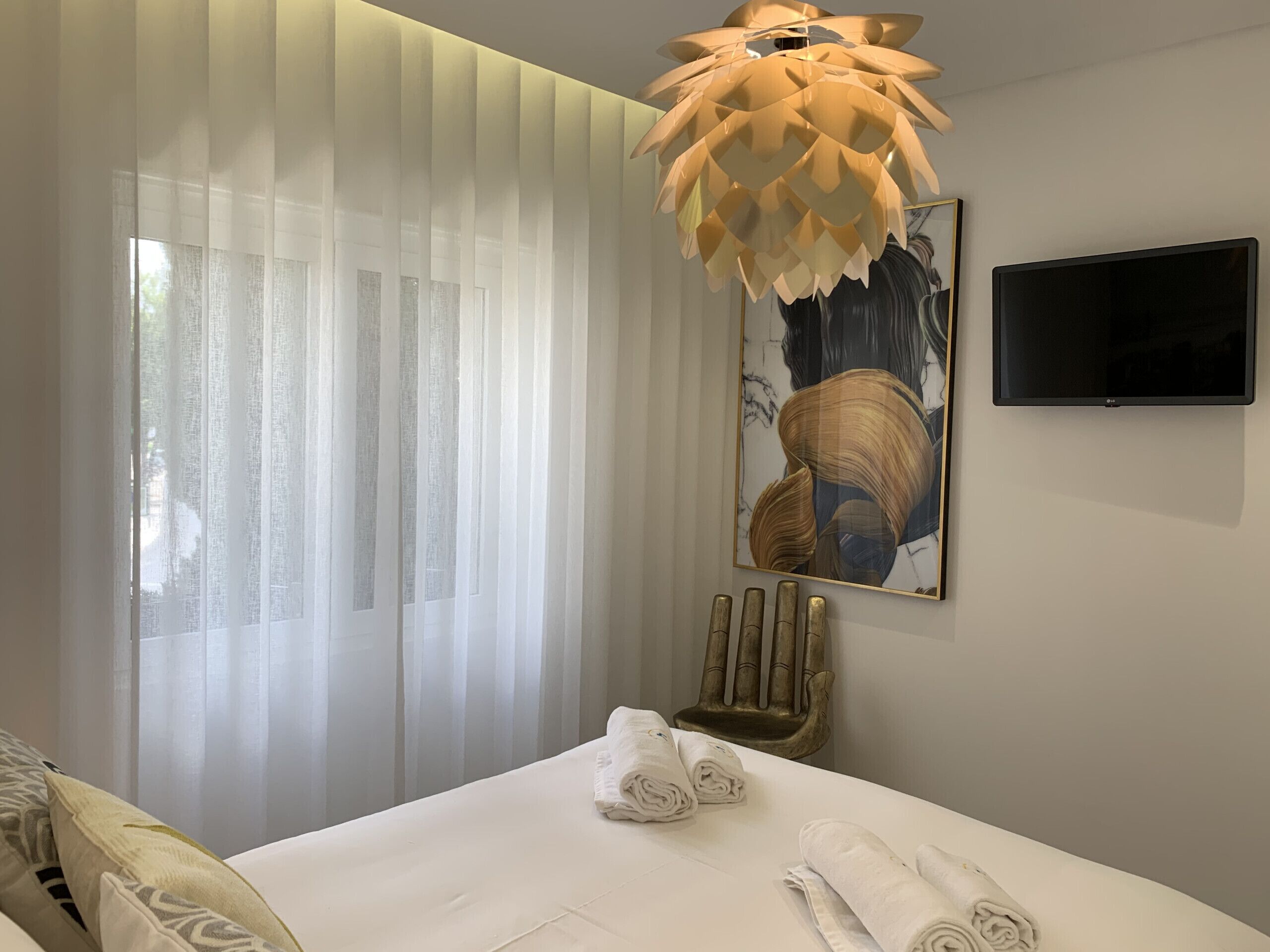 A hotel room with a bed, a television mounted on the wall, and a large abstract painting above the bed.
