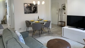 Ett modernt vardagsrum med en grå soffa, ett matbord dukat med gula tallrikar och glas, en platt-TV och en modern kristallkrona.