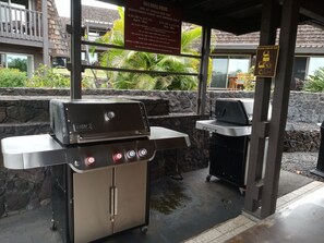 An outdoor grill area with a gas grill and a charcoal grill, surrounded by stone walls and greenery. - Beautiful 1-bedroom condo at Punalu'u black sand beach (Pahala)