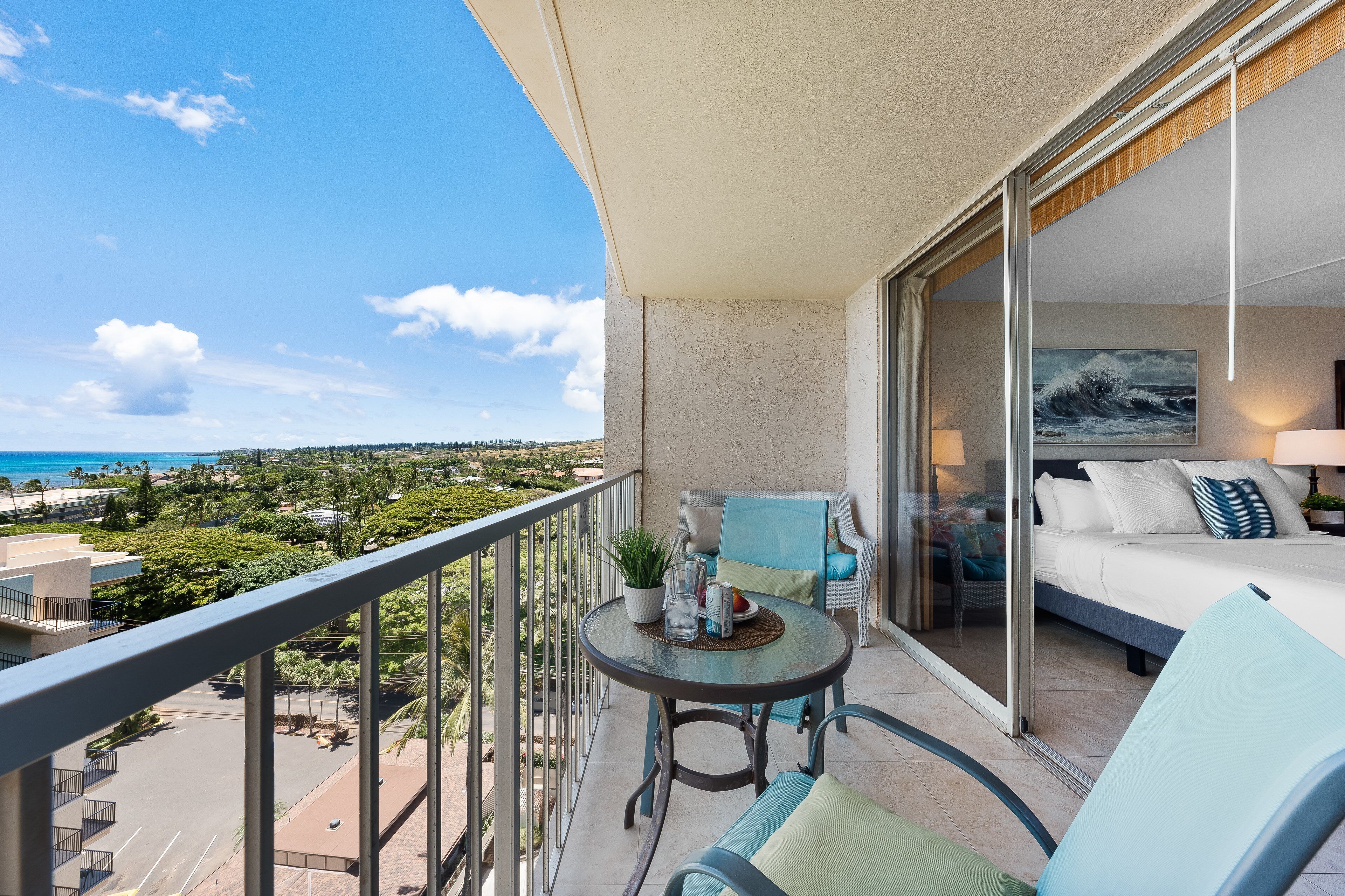 A balcony with a glass table, chairs, and a bed with a view of the ocean.