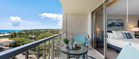 A balcony with a glass table, chairs, and a bed with a view of the ocean.