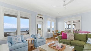 A spacious living room with a view of the ocean, featuring a light blue sofa, a green sofa, and a coffee table with a basket. - 4BR Oceanfront - Amazing Sunsets! Amenity Access incl. (Seabrook Island)