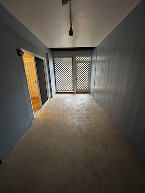 Ein Korridor mit Betonboden, Deckenventilator und zwei Holztüren mit Gitterwerk.