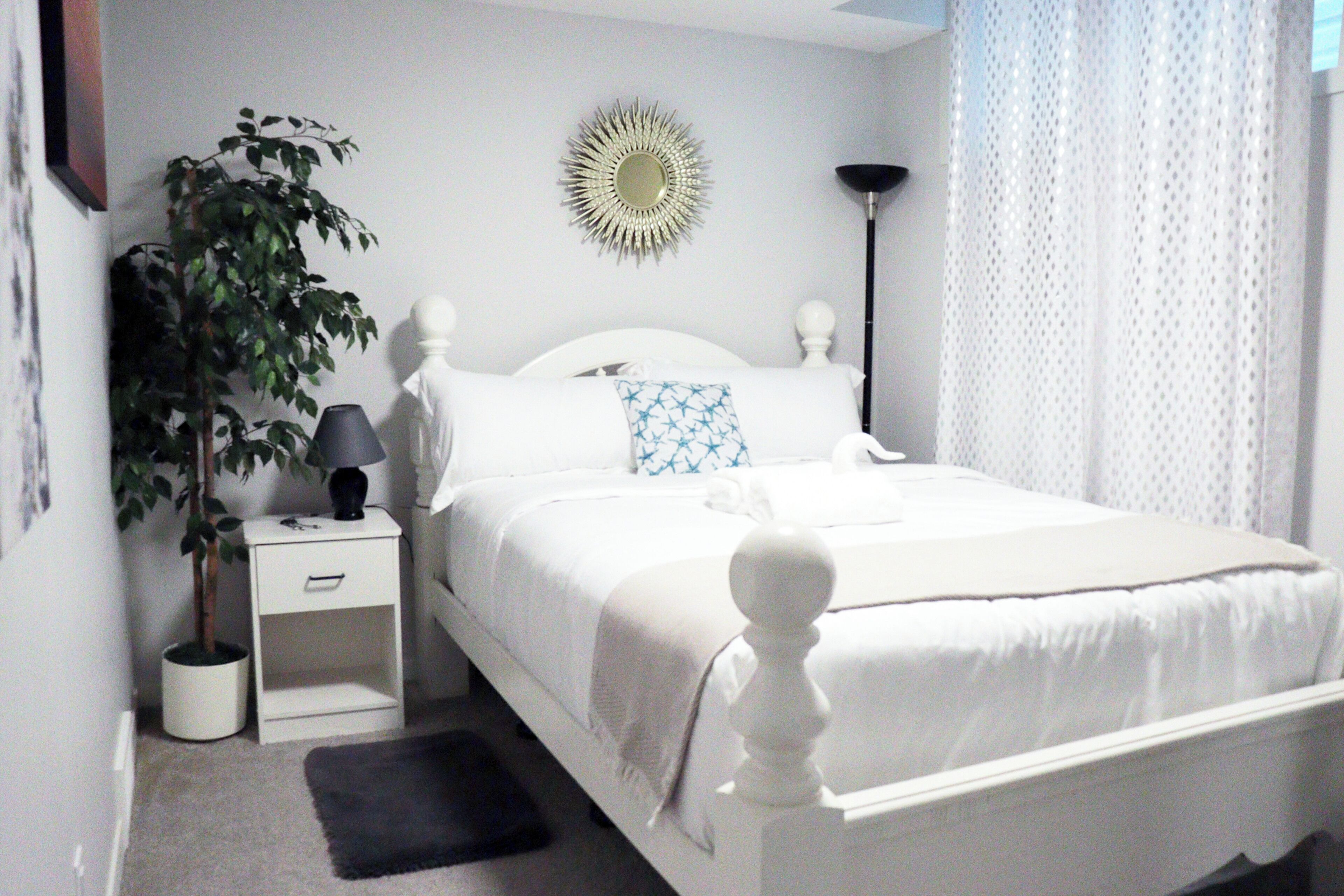 A neatly arranged bedroom with a bed, bedside table, lamp, and a potted plant.