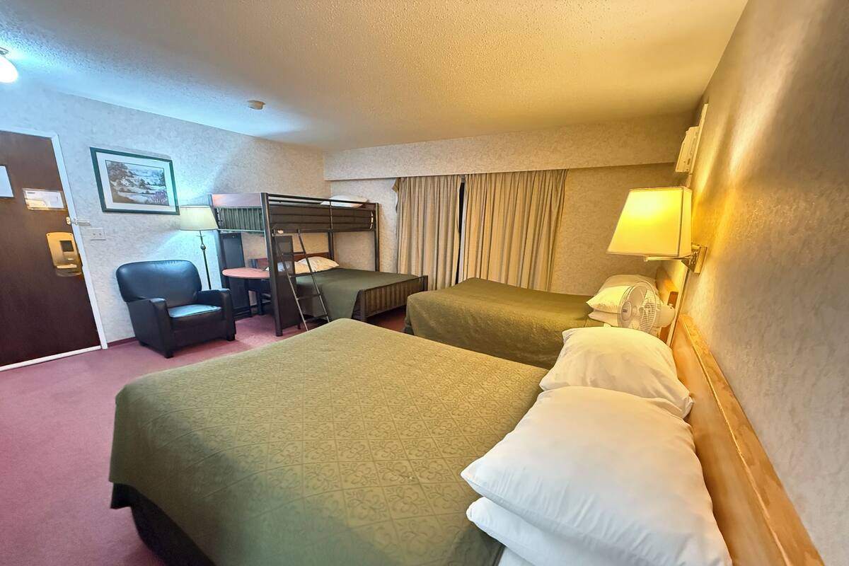 Une chambre d’hôtel avec deux lits, un bureau, une chaise, une échelle et un ventilateur.