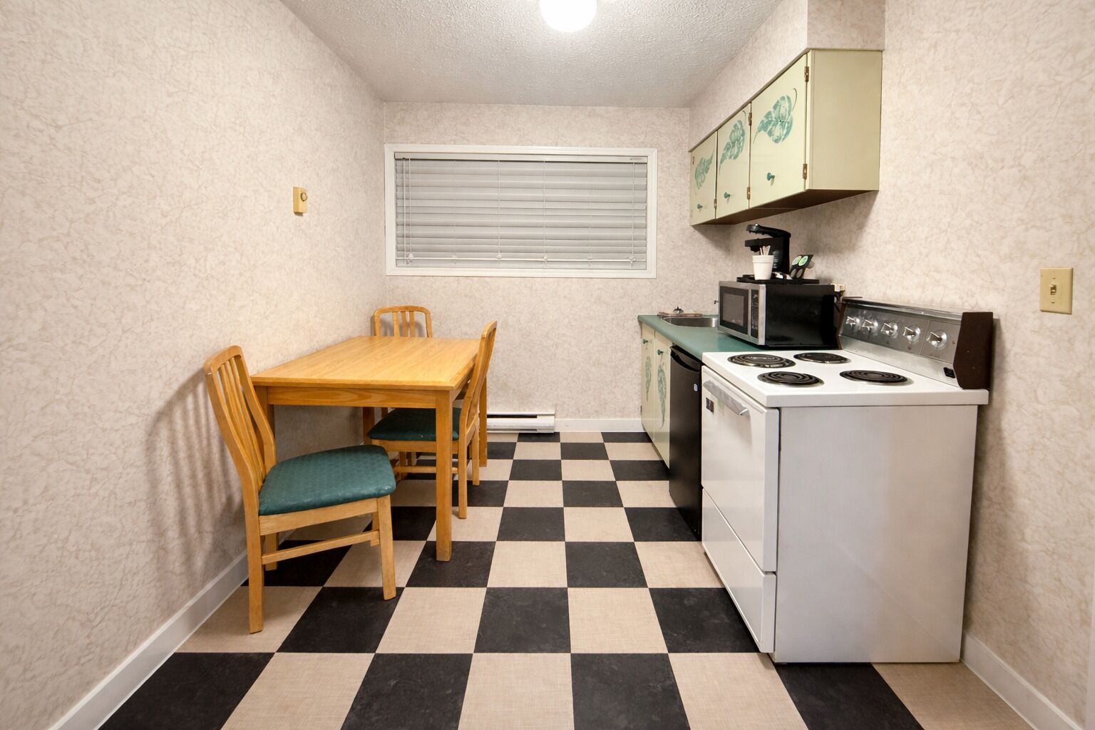 Una cocina compacta con piso a cuadros, una mesa de comedor de madera con sillas, un microondas y una estufa.