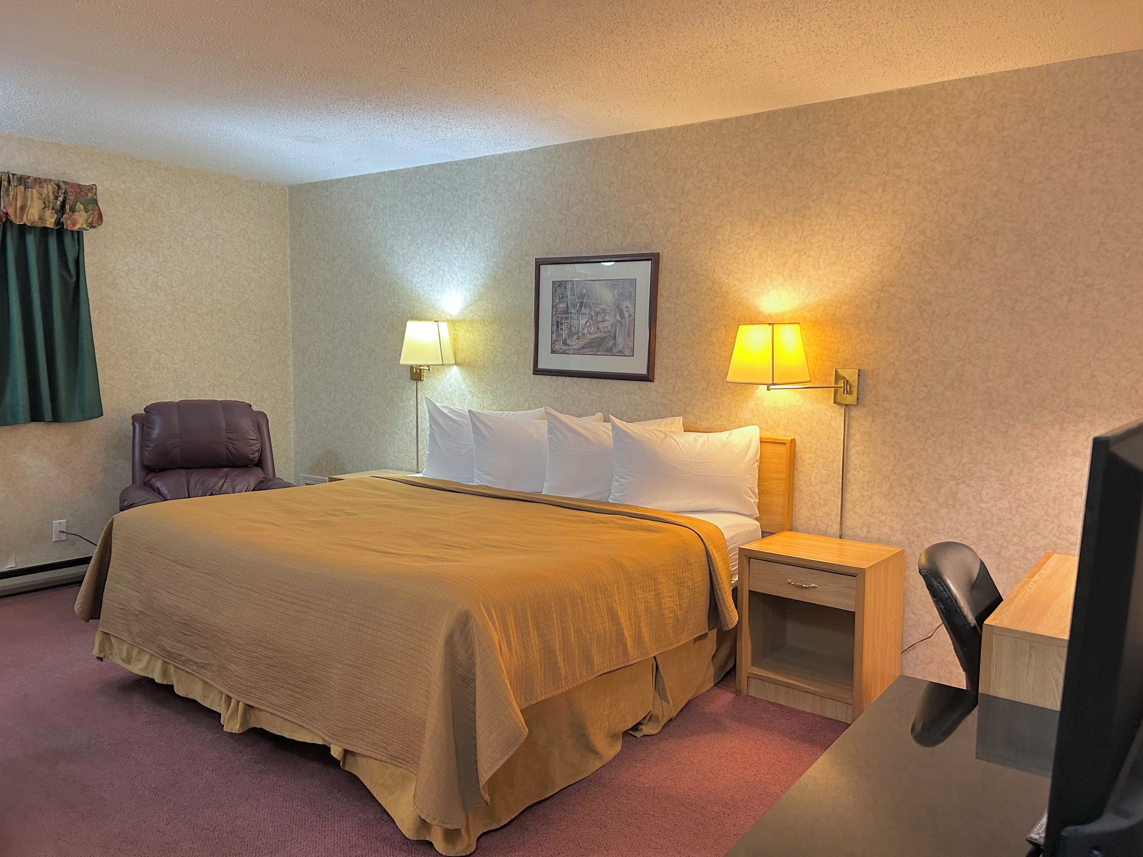 Una habitación de hotel con una cama, dos lámparas de noche, una silla, un escritorio y un televisor.