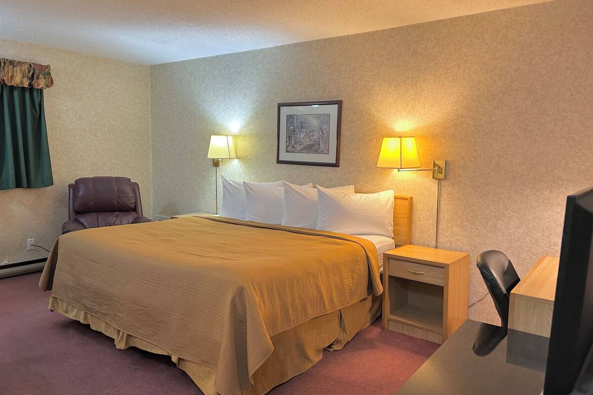 Une chambre d’hôtel comprenant un lit, deux lampes de chevet, une chaise, un bureau et un téléviseur.