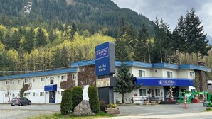 A hotel with a blue roof, a sign for an indoor pool and hot tub, and a mountain backdrop. - Rychter Hotel Hope (Hope)