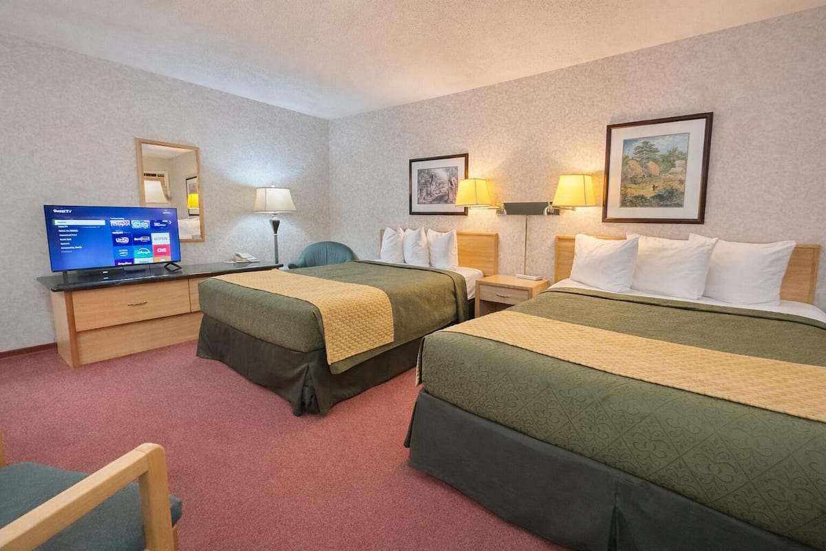 Une chambre d’hôtel avec deux lits, un bureau avec une télévision et deux lampes de chevet.