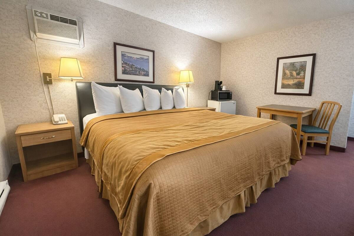 Une chambre d’hôtel avec un grand lit, deux tables de chevet, une chaise, un bureau, un four à micro-ondes et deux tableaux encadrés accrochés aux murs.