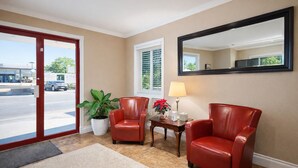 Un hall d’hôtel avec deux fauteuils en cuir rouge, une plante en pot, une table avec une lampe et un grand miroir au mur.