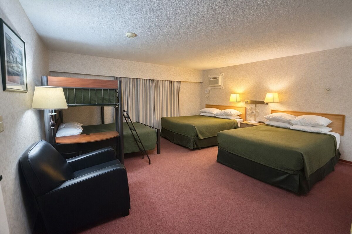 Ett hotellrum med två sängar, ett skrivbord med en stol, en golvfläkt och en väggmonterad luftkonditioneringsanläggning.
