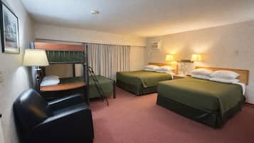 A hotel room with two beds, a desk with a chair, a standing fan, and a wall-mounted air conditioner.