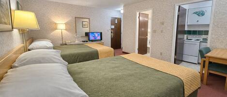 A hotel room with two beds, a television, a desk, and a kitchenette.