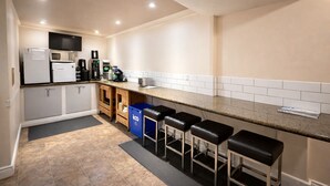 Une cuisine compacte comprenant un plan de travail, un réfrigérateur, une machine à café et une poubelle.
