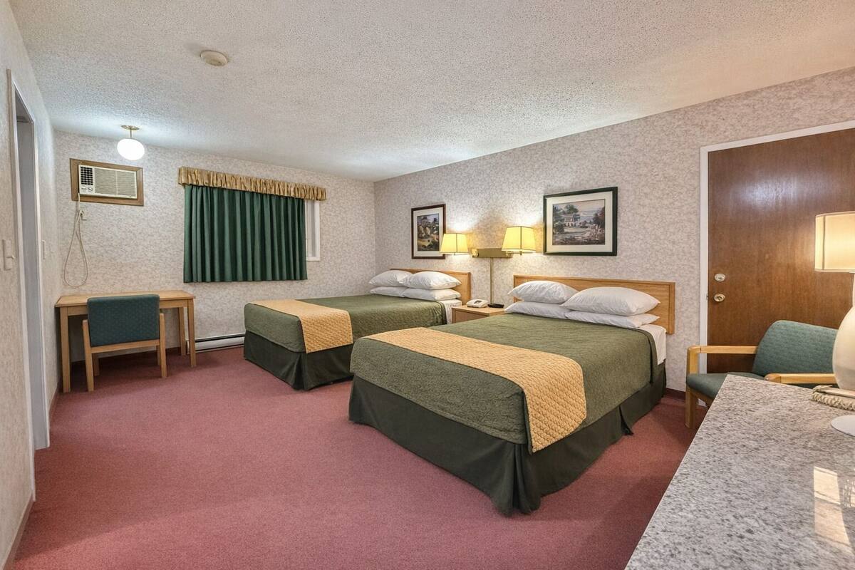 Une chambre d’hôtel avec deux lits simples, un bureau, une chaise, une petite table, une lampe et une porte.