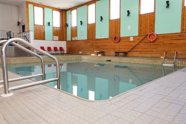 An indoor swimming pool with a tiled floor, wooden walls, and a metal pool ladder.