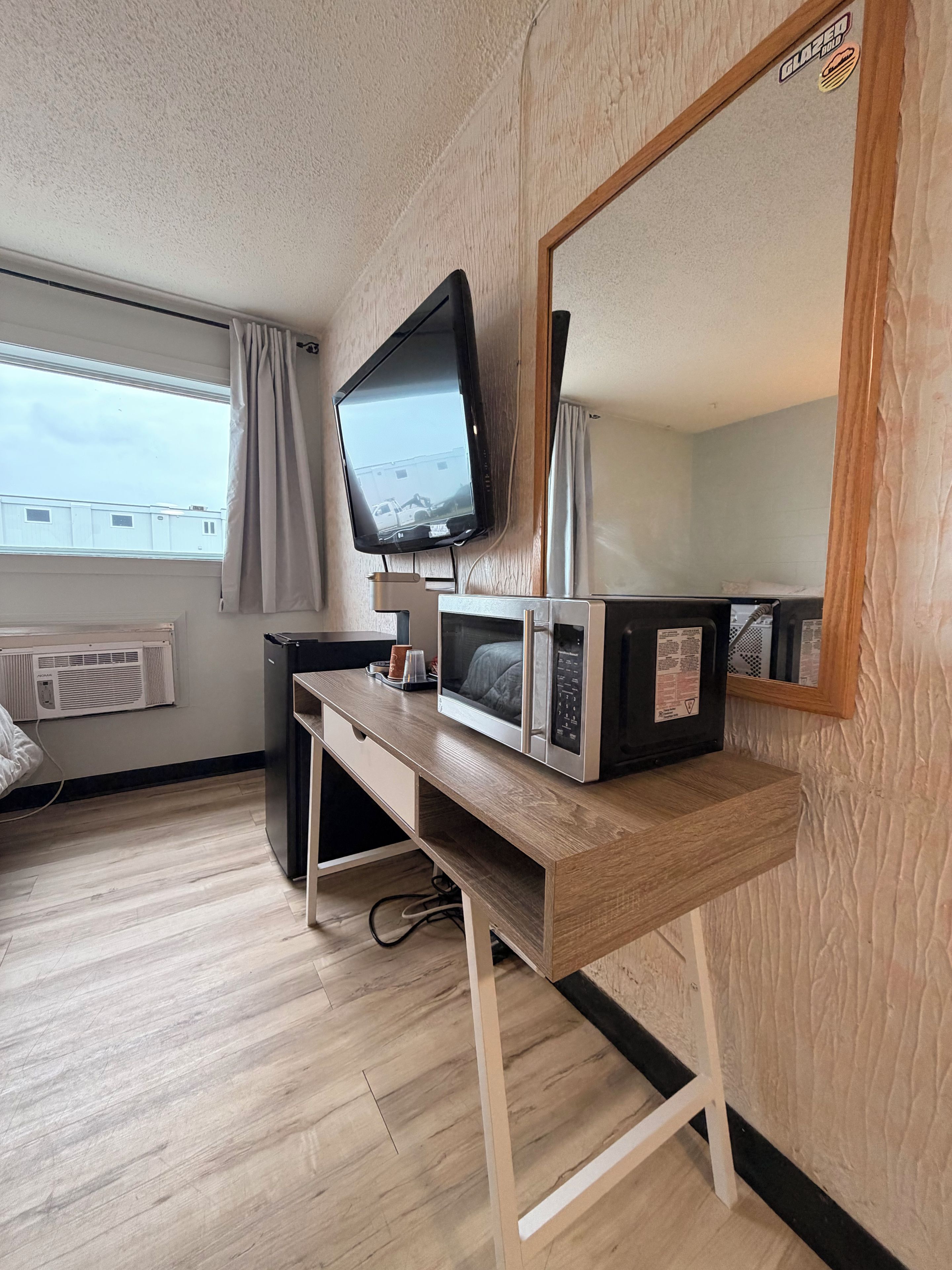 A room with a wooden desk, a television, a microwave, and a large mirror.