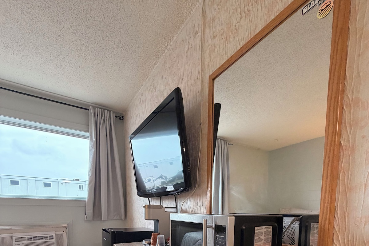 A room with a wooden desk, a television, a microwave, and a large mirror.