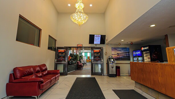 Een hotel lobby met een rode leren bank, een houten receptiebalie, een kroonluchter, een televisiescherm en een automaat voor Pepsi.