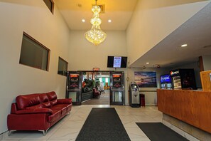 A hotel lobby with a red leather sofa, a wooden reception desk, a chandelier, a television screen, and a Pepsi vending machine.