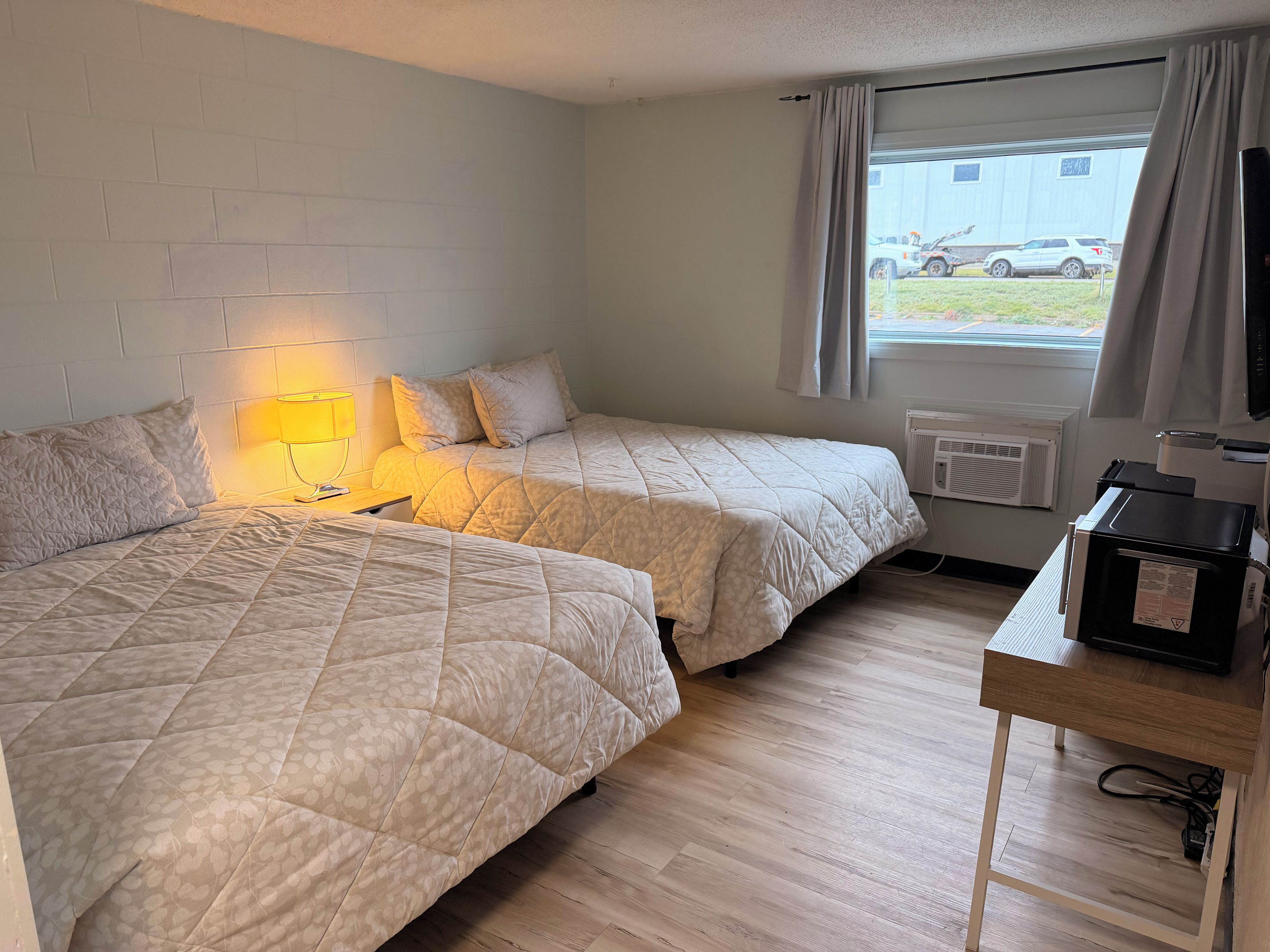 Une chambre d’hôtel avec deux lits, une table de chevet avec une lampe, un radiateur et une fenêtre avec des rideaux.